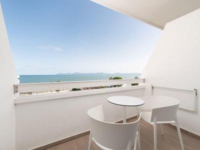 Balcon avec deux chaises blanches et tables donnant sur la mer sous un ciel bleu.