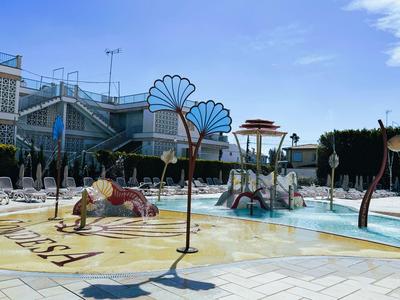 Bambini si divertono nell'area piscina bassa di un hotel con scivoli e ombrelloni.