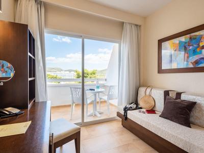 Chambre d'hôtel lumineuse avec canapé, bureau et balcon donnant sur l'eau et la verdure.