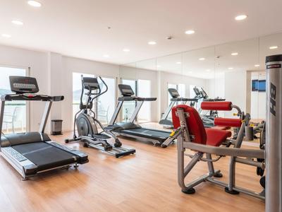 Palestra luminosa con tapis roulant, biciclette e attrezzi per la forza su pavimento in legno.