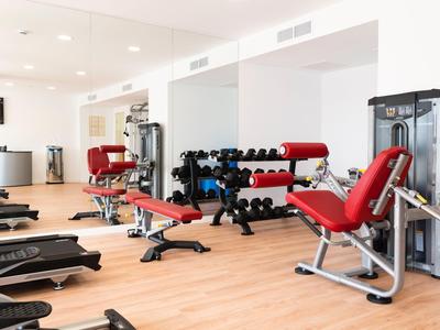 Palestra moderna con attrezzi rossi e manubri su pavimento in legno chiaro