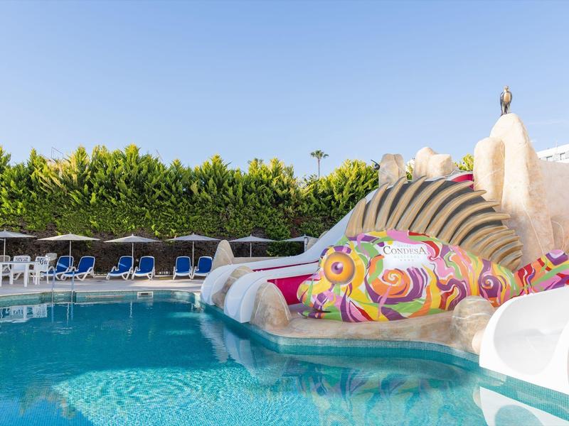 Piscine pour enfants avec un toboggan aquatique en forme de poisson coloré et des chaises longues en arrière-plan.