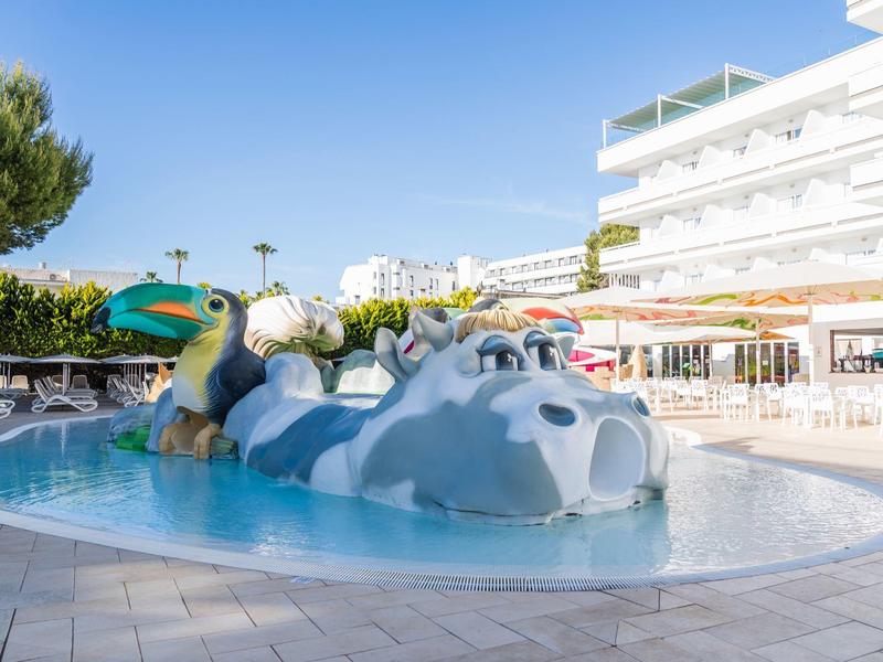 Piscine pour enfants avec une grande structure de jeu d'eau hippopotame blanche à l'extérieur près d'un hôtel.