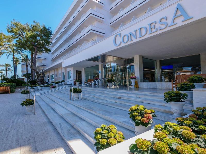 Entrée d'hôtel moderne avec un large escalier et des parterres de fleurs par temps ensoleillé.
