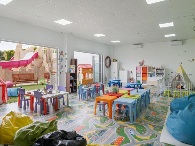 Salle de jeux pour enfants lumineuse avec petites tables, chaises et poufs dans un espace coloré.