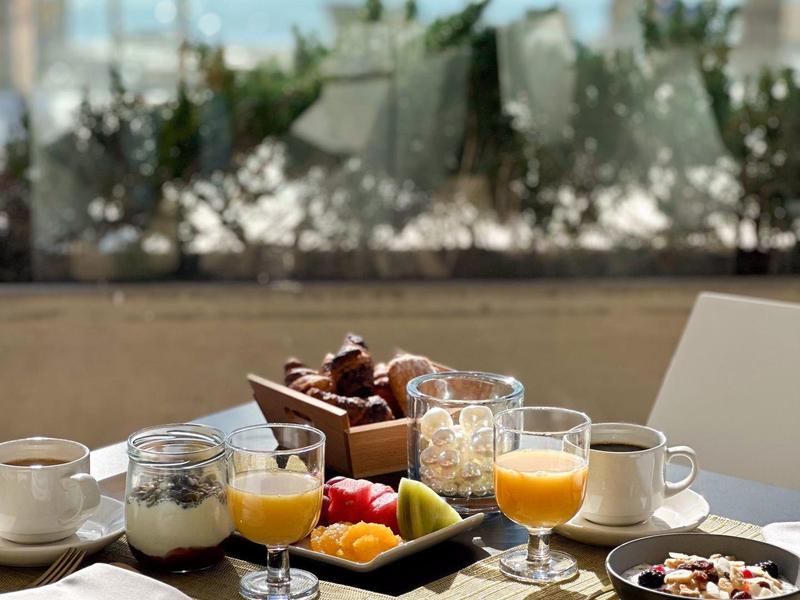 Table de petit déjeuner avec jus d'orange, assiette de fruits et café avec vue sur la mer et parasols.