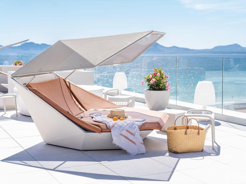Chaise longue moderne avec pare-soleil sur une terrasse avec vue sur la mer et les montagnes.
