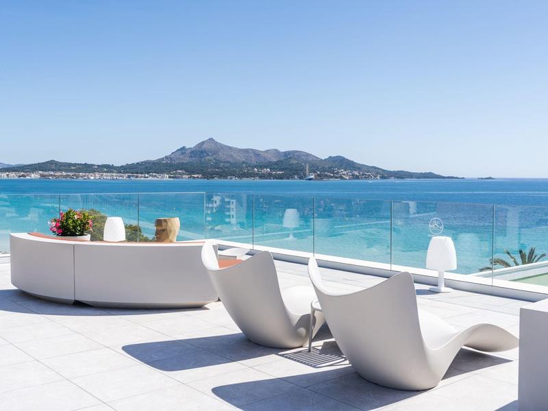 Mobilier de lounge moderne sur une terrasse avec vue sur la mer et montagnes en arrière-plan.