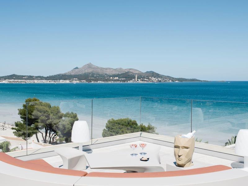 Vue depuis une terrasse d'hôtel sur la mer avec une île et des montagnes sous un ciel clair.
