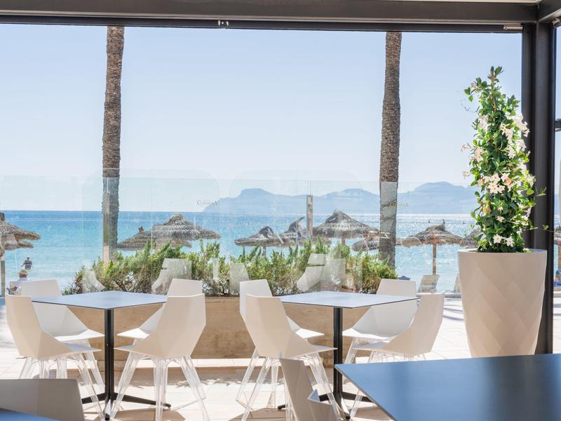 Terrasse avec chaises blanches et tables donnant sur la mer et des palmiers en dessous.