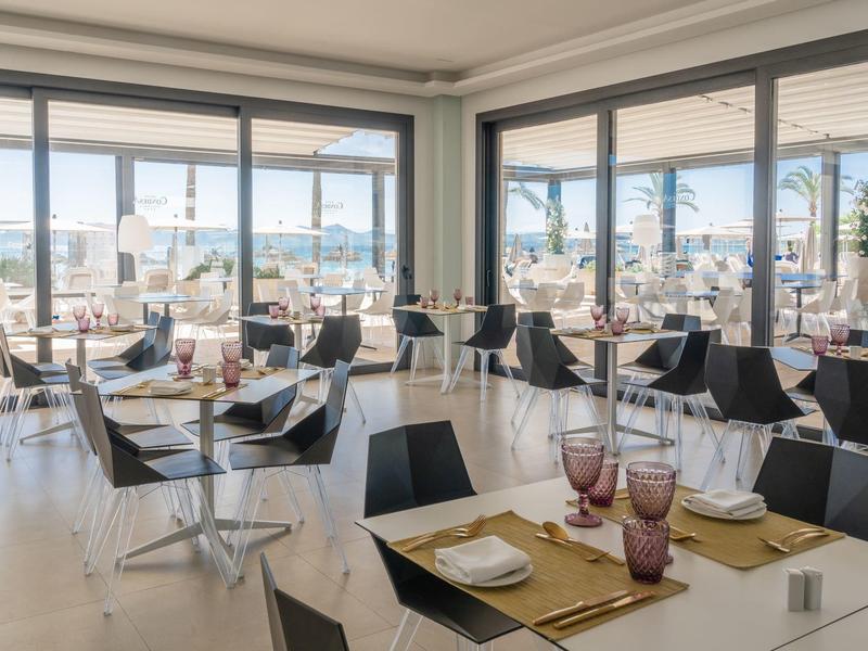 Restaurant moderne avec grandes fenêtres et vue sur la mer, ambiance lumineuse et accueillante.