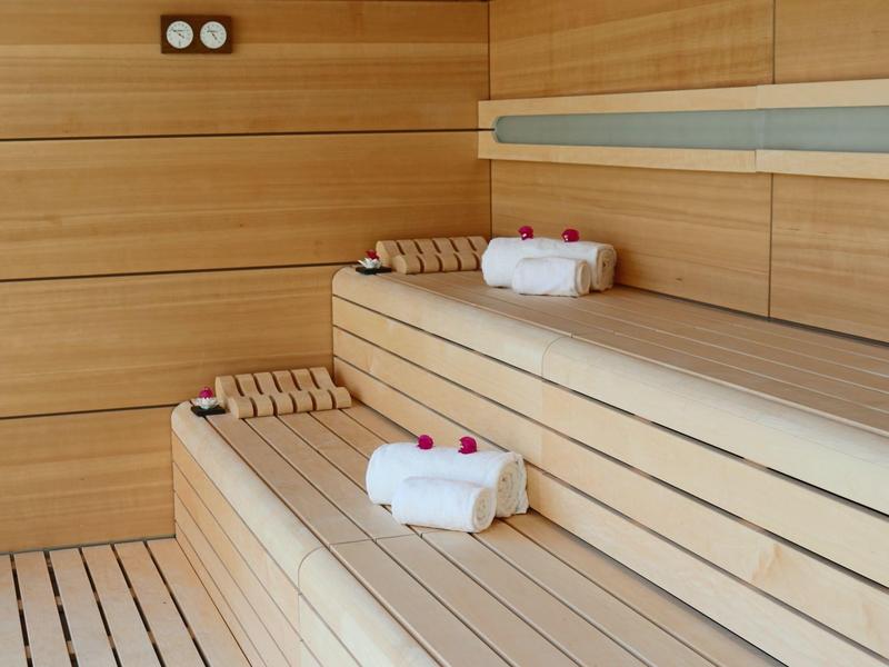 Sauna avec des bancs en bois clair, des serviettes et de petites bouteilles sur les sièges.