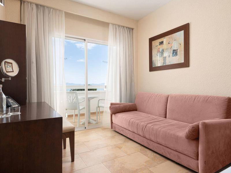 Salon confortable avec canapé rose, télévision et balcon avec vue sur la mer.