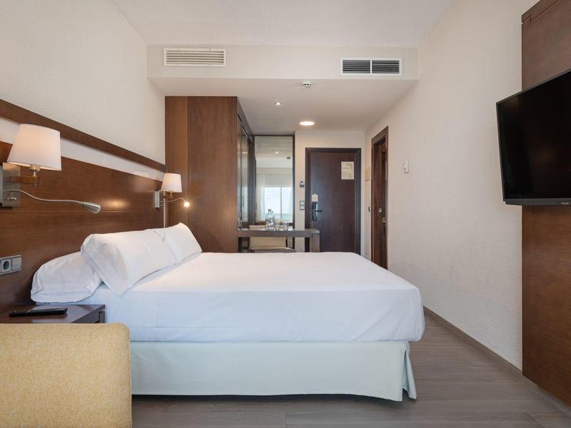 Chambre d'hôtel moderne avec grand lit, lampes murales et télévision à écran plat.