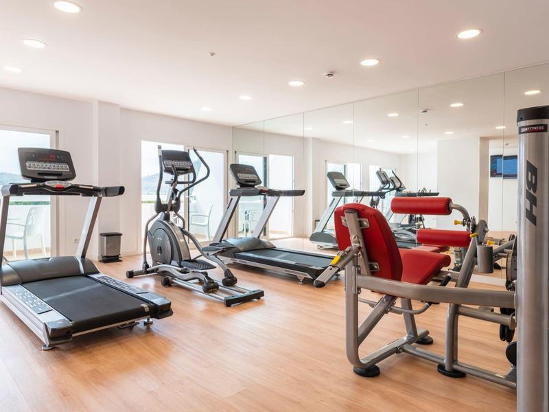 Salle de sport bien éclairée avec tapis de course, appareils elliptiques et machines de musculation sur sol en bois.