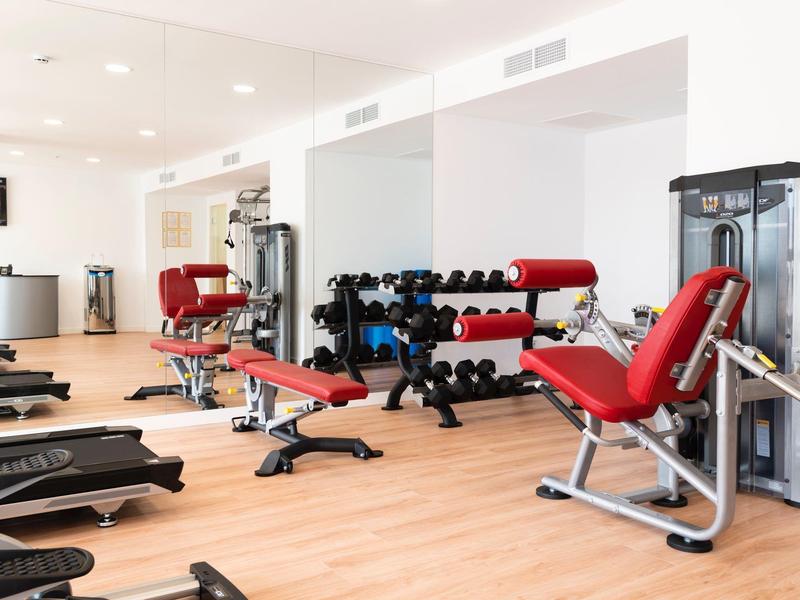 Salle de sport moderne avec équipements d'entraînement rouges et haltères sur sol en bois.