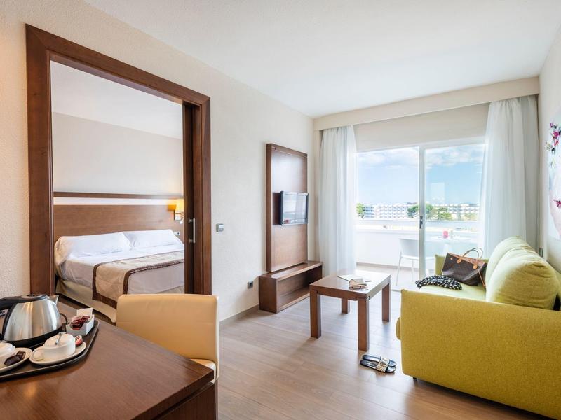 Chambre d'hôtel lumineuse avec coin salon confortable, lit et balcon avec vue sur la mer.