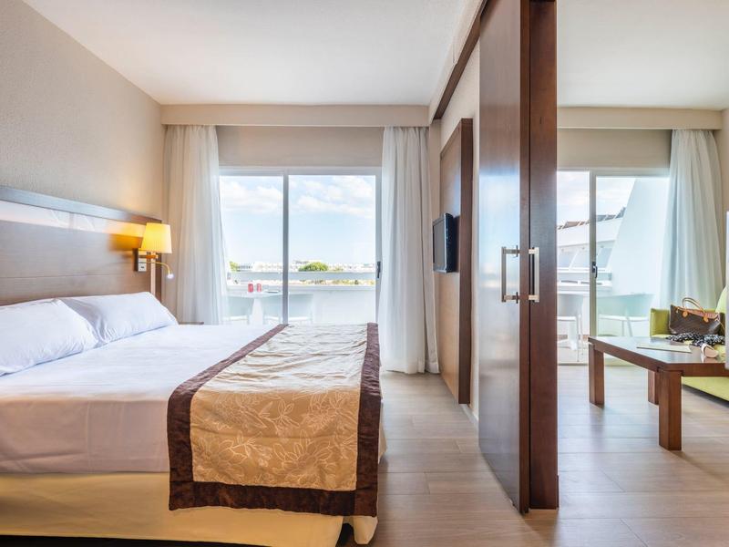 Chambre d'hôtel lumineuse avec grand lit et balcon avec vue sur la mer.