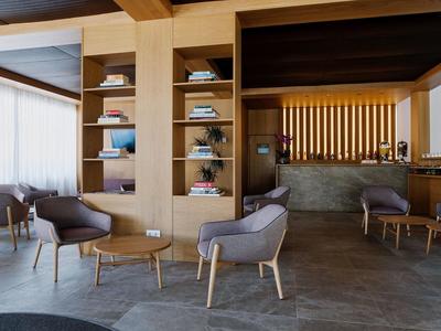 Moderner Lounge-Bereich mit Holzregalen, grauen Sesseln, kleinen Tischen und großem Fenster.