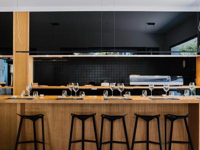 Moderne Bar mit hellem Holz, schwarzen Hockern und einer langen Spiegelwand hinter der Theke.