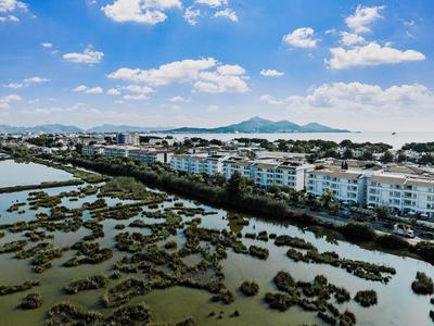 Wohnhäuser am Küstenrand mit Wattlandschaft und Bergen im Hintergrund unter blauem Himmel.