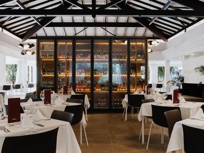 Elegantes Restaurant mit weißen Tischdecken, schwarzen Stühlen und großer Weinvitrine im Hintergrund.