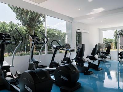 Modern gym with cardio machines and large windows overlooking greenery.