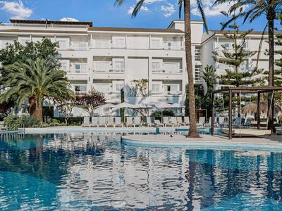 Hotel mit mehrstöckigem Gebäude, großem Pool, Palmen und Liegestühlen bei klarem Himmel.