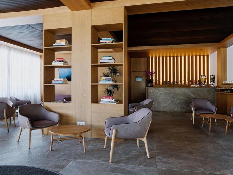 Moderner Lounge-Bereich mit Holzregalen, grauen Sesseln, kleinen Tischen und großem Fenster.