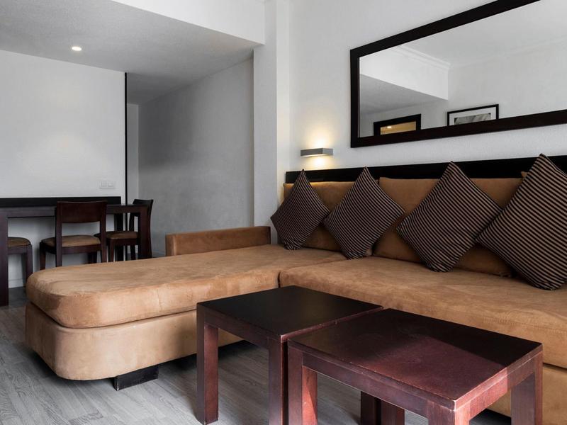 Modernes Wohnzimmer mit braquem Ecksofa, dunklen Holztischen und großem Wandspiegel.