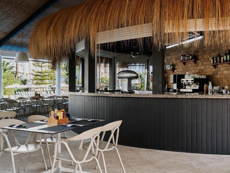Modernes Außencafé mit schwarzer Theke, weißen Stühlen und natürlichen Strohdach-Dekor.