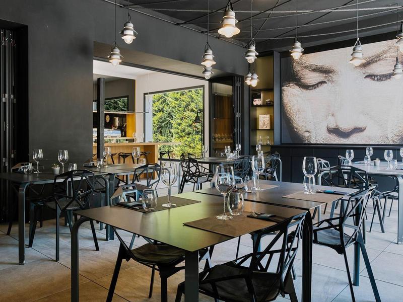 Modernes Restaurant mit Holz- und Metallmöbeln, großen Fenstern und einem großen Gemälde einer Frauenportraitwand.