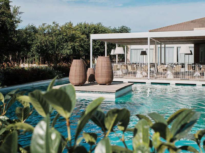 Moderner Außenpool mit großer Terrasse, zwei großen Vasen und grünen Pflanzen im Vordergrund.