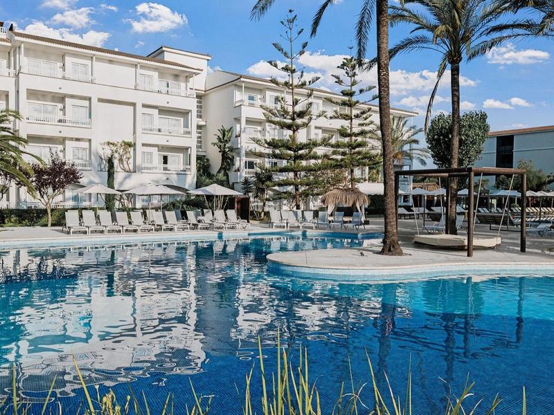 Moderner Hotelpool mit Palmen, Liegestühlen und blauem Wasser unter blauem Himmel.
