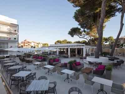 Espace extérieur d'un hôtel avec de nombreuses tables, chaises et sièges lounge sous les arbres.