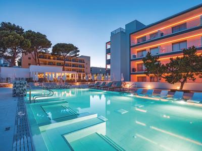 Hotel moderno con piscina exterior iluminada y tumbonas al anochecer