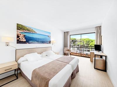 Chambre d'hôtel lumineuse avec lit double, balcon donnant sur des arbres et mobilier moderne.