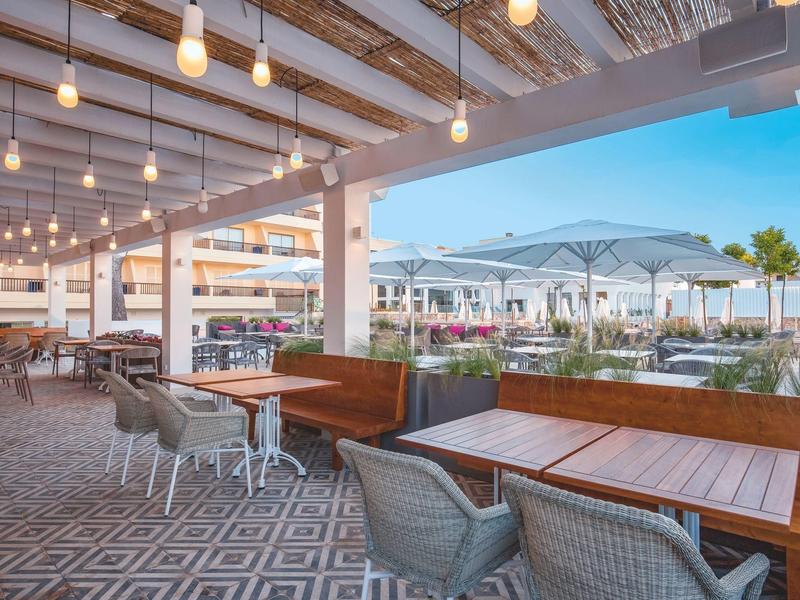 Espace extérieur moderne d'un hôtel avec tables, chaises et éclairage chaleureux en plein jour.