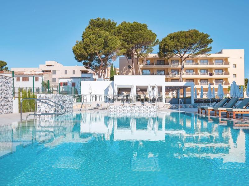 Complexe hôtelier moderne avec piscine, chaises longues et grands arbres sous un ciel clair.