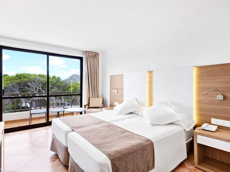 Chambre d'hôtel moderne avec lit double, balcon et vue sur des arbres verts et des montagnes.