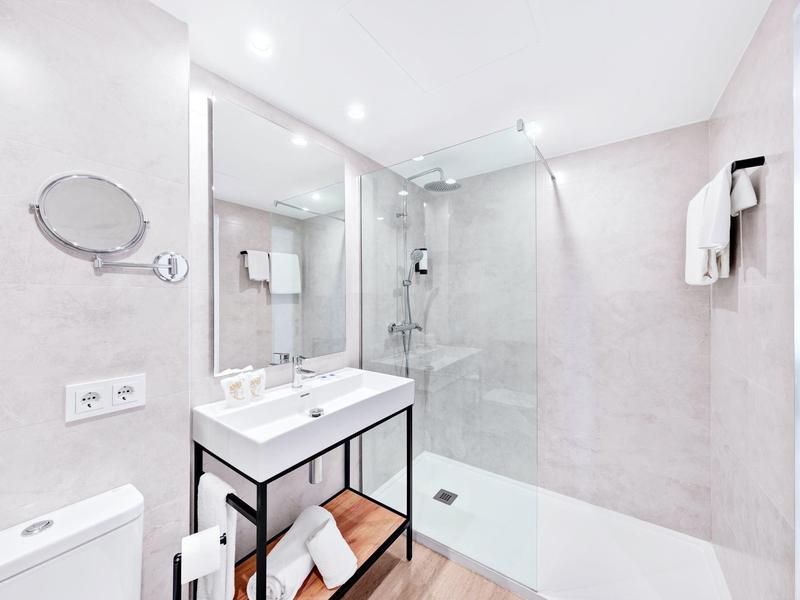 Salle de bain moderne avec grande douche à l'italienne, lavabo et toilette dans des tons clairs.