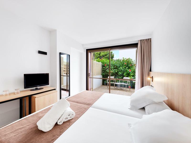 Chambre d'hôtel moderne avec deux lits simples, télévision et accès à une terrasse avec vue sur la verdure.