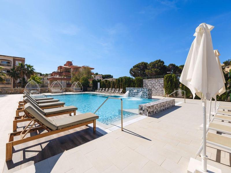 Piscine d'hôtel moderne avec chaises longues et parasols sous un ciel dégagé.