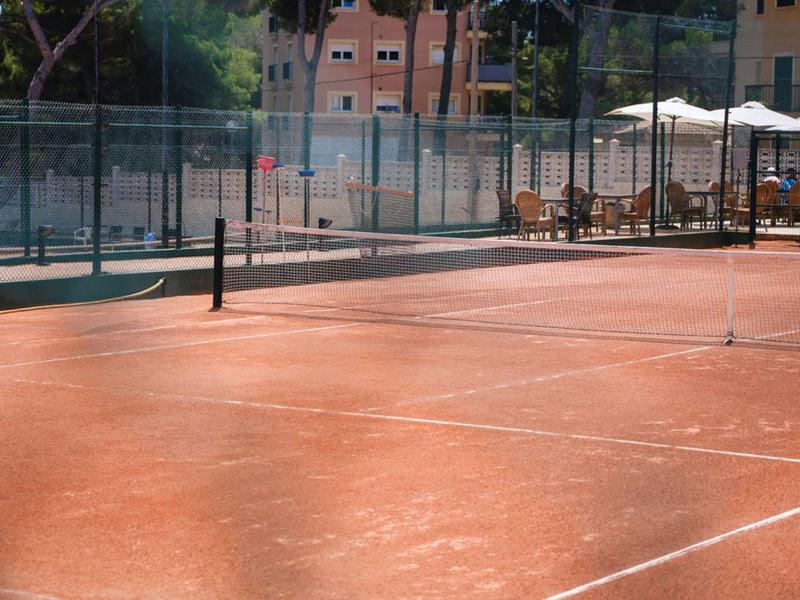 Court de tennis vide avec surface rouge et clôture dans un cadre ensoleillé.