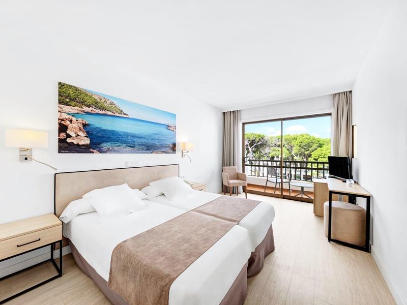 Chambre d'hôtel lumineuse avec lit double, balcon donnant sur des arbres et mobilier moderne.