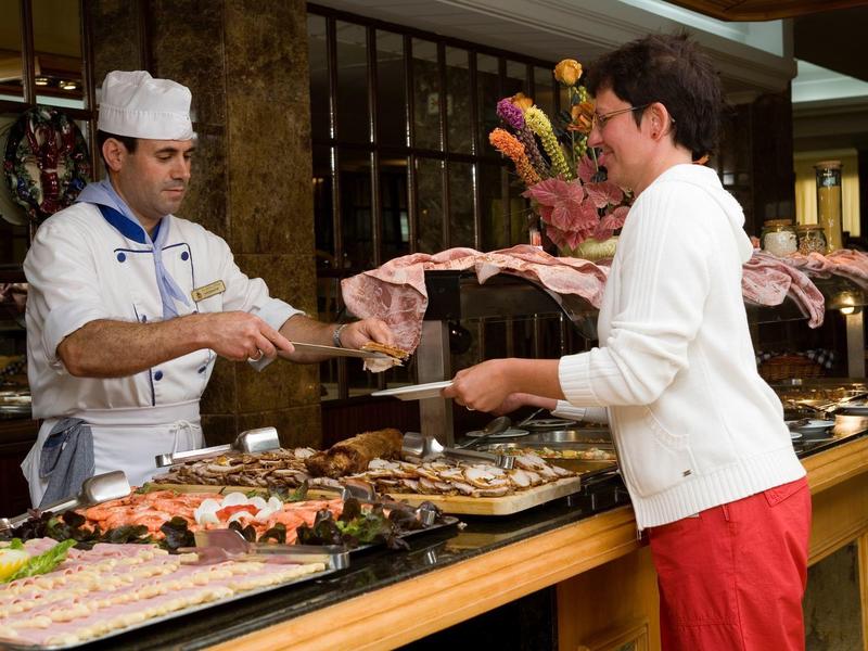 Kucharz podaje jedzenie gościowi przy bufecie w hotelowej restauracji.