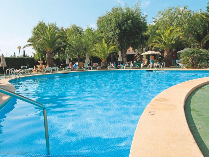 Okrągły hotelowy basen z poręczą, otoczony leżakami i palmami.