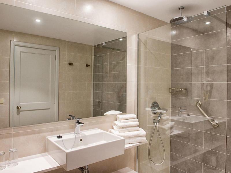 Nowoczesna łazienka z umywalką, dużym lustrem i prysznicem z szarymi płytkami.