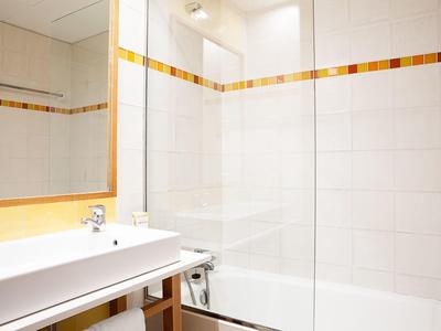 Bagno luminoso con vasca da bagno bianca, lavabo e accenti arancioni sulle piastrelle.