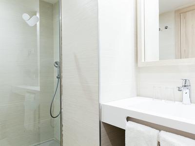 Bagno moderno con doccia, lavabo e asciugamani in bianco e grigio chiaro.